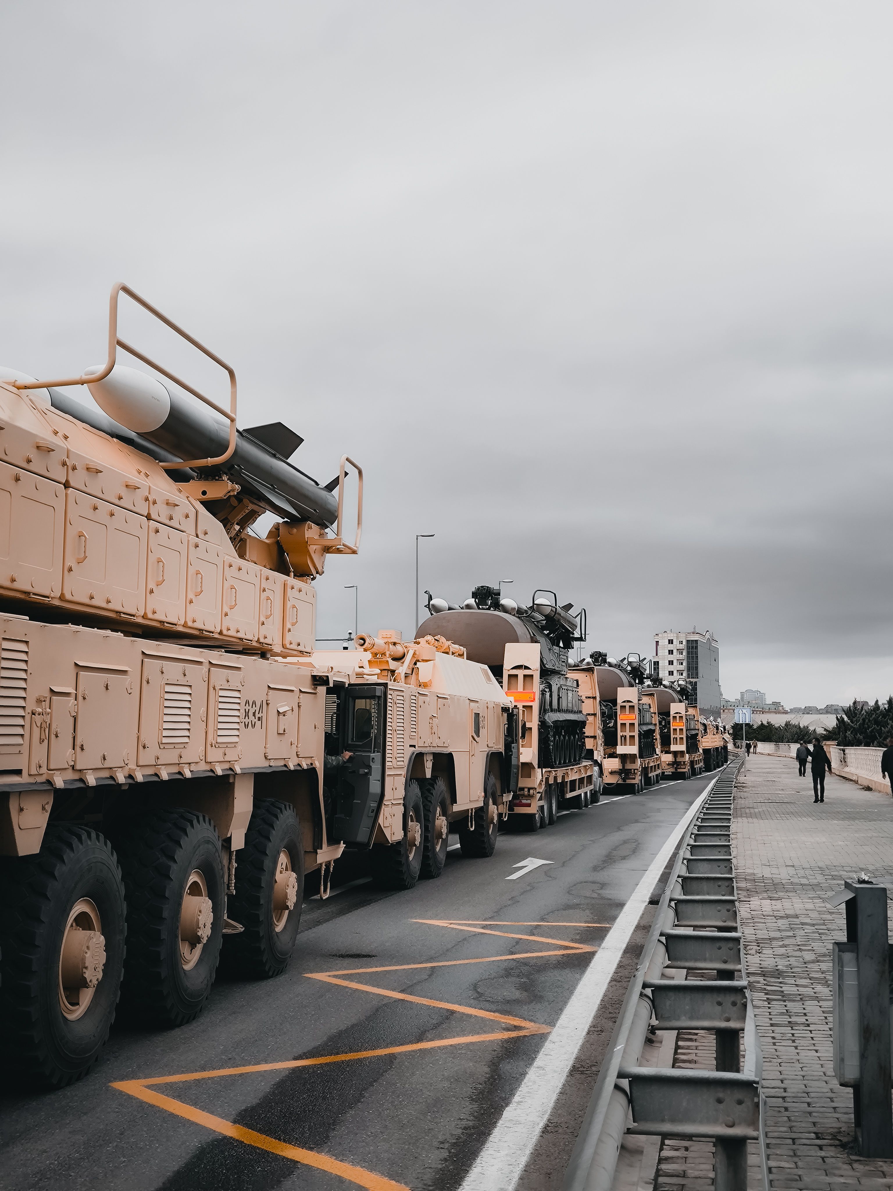 A line of mobile military vehicles carrying missile launch systems, parked along a city road.