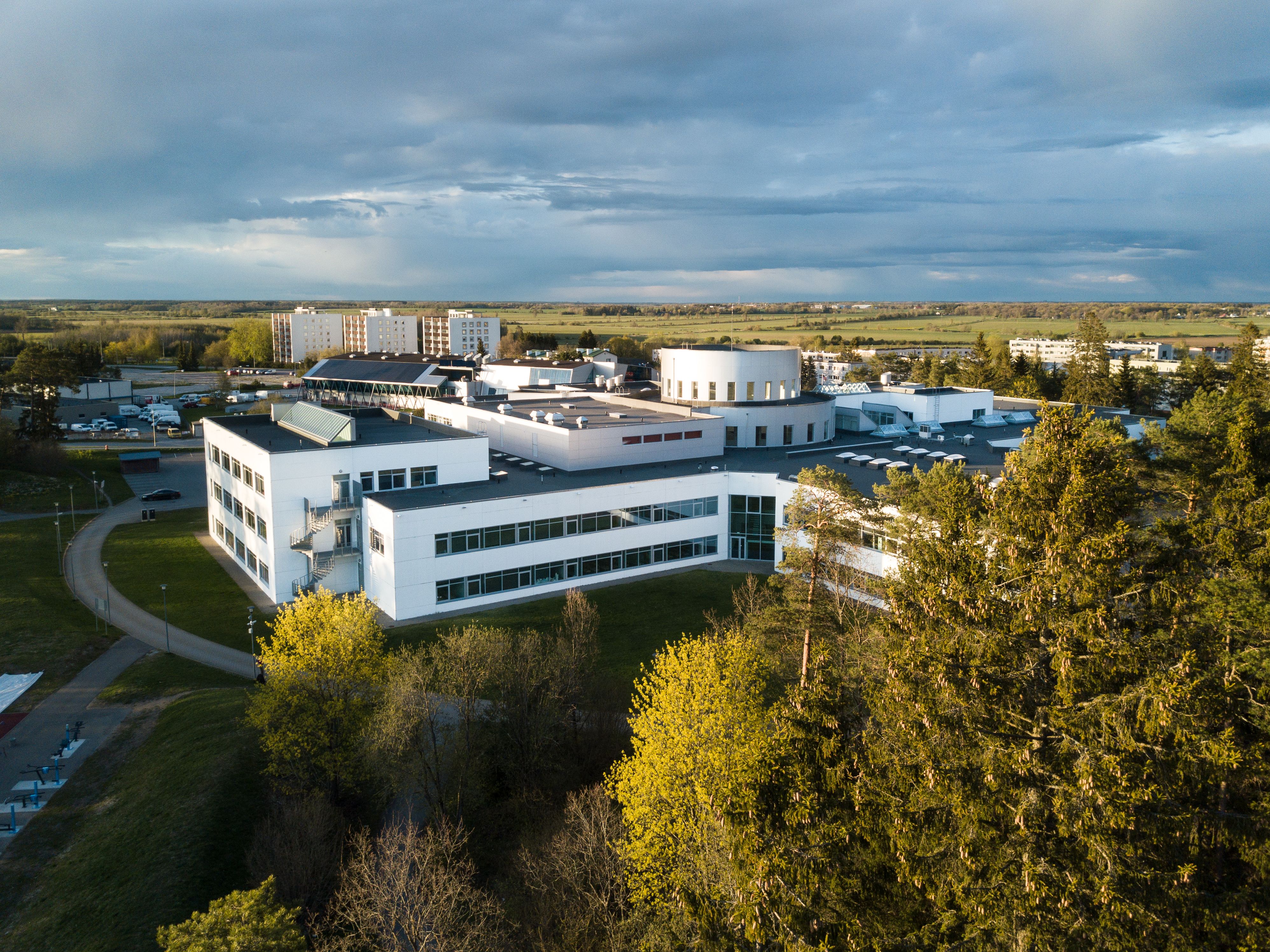 An aerial view of a low-rise office building complex surrounded by lawns, trees, and a parking area.
